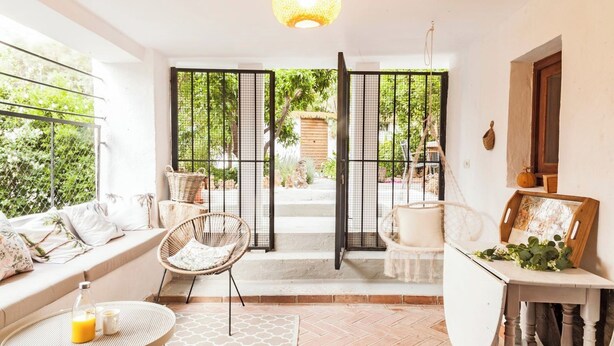 A cozy interior with a seating area, a dining table, and a view through a gate to a garden.