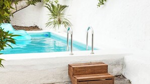 A swimming pool with two metal ladders, surrounded by white walls and a small wooden bench.
