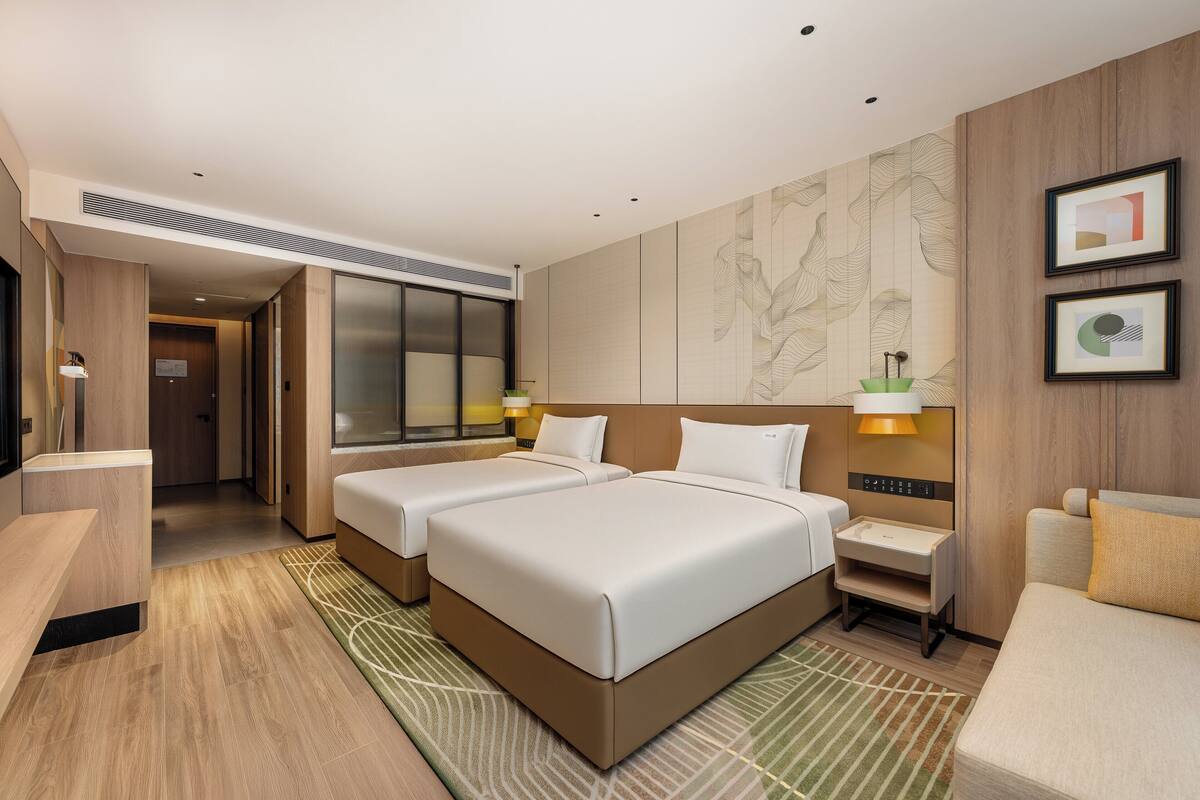 Habitación de hotel con dos camas, un escritorio y una silla. Cuenta con un ventanal grande y una obra de arte colgada en la pared.
