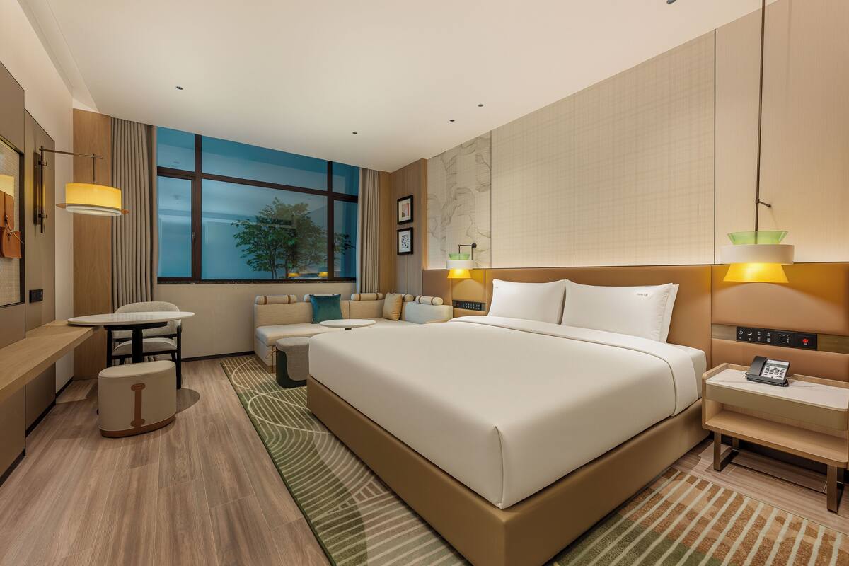 Una habitación de hotel moderna con una cama grande, un escritorio, un sofá y vistas al exterior a través de un amplio ventanal.