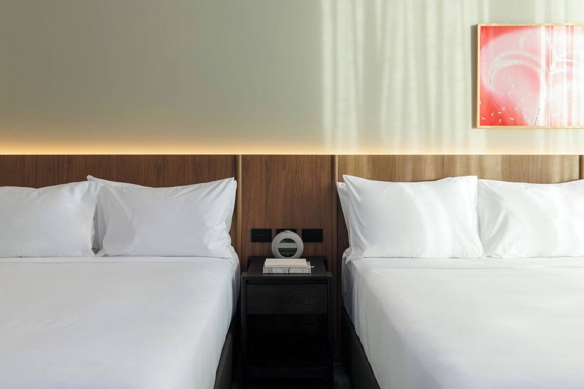 Une chambre d’hôtel avec deux lits, une tête de lit en bois, une table de chevet avec une lampe et une œuvre d’art abstraite accrochée au mur.