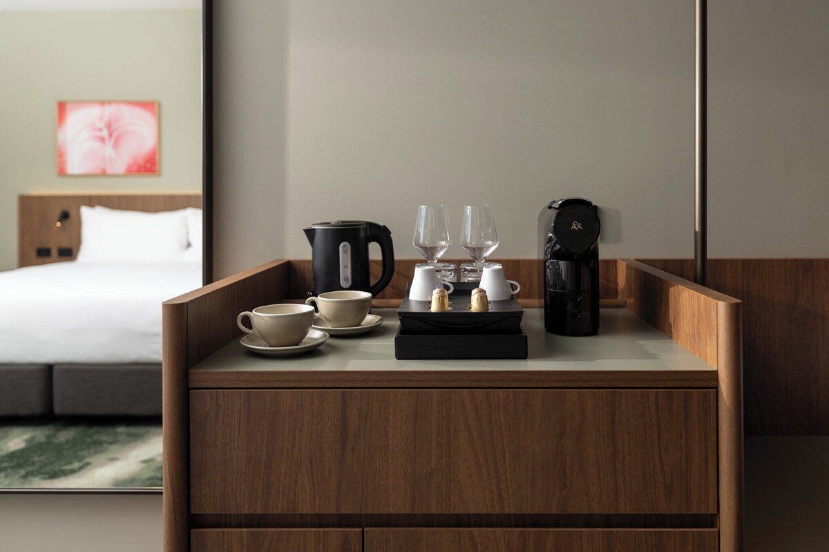 Habitación de hotel con una mesita de madera que sostiene una tetera, dos vasos, una taza y una cafetera.
