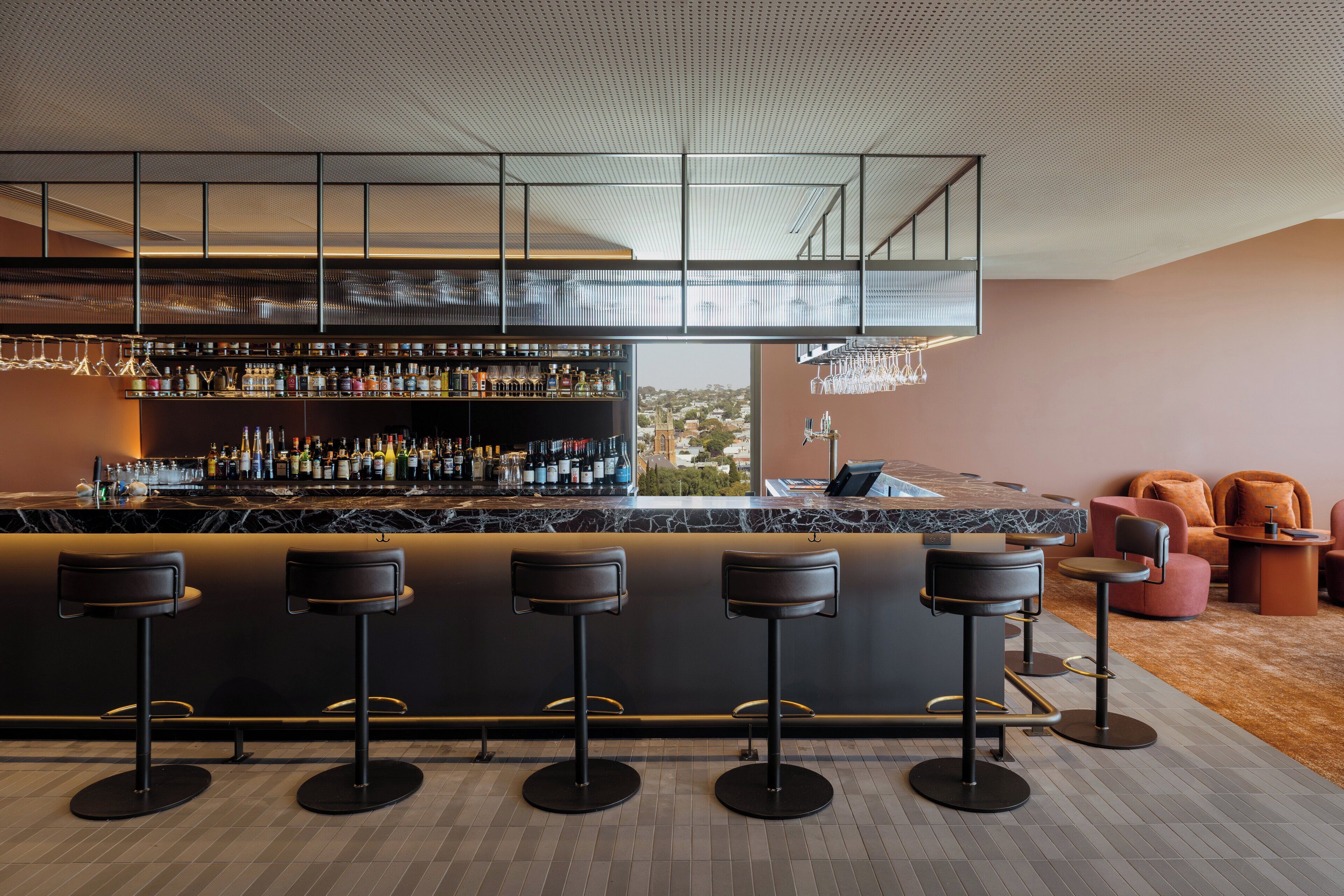 A modern bar area with a high ceiling, a marble countertop, and multiple stools.