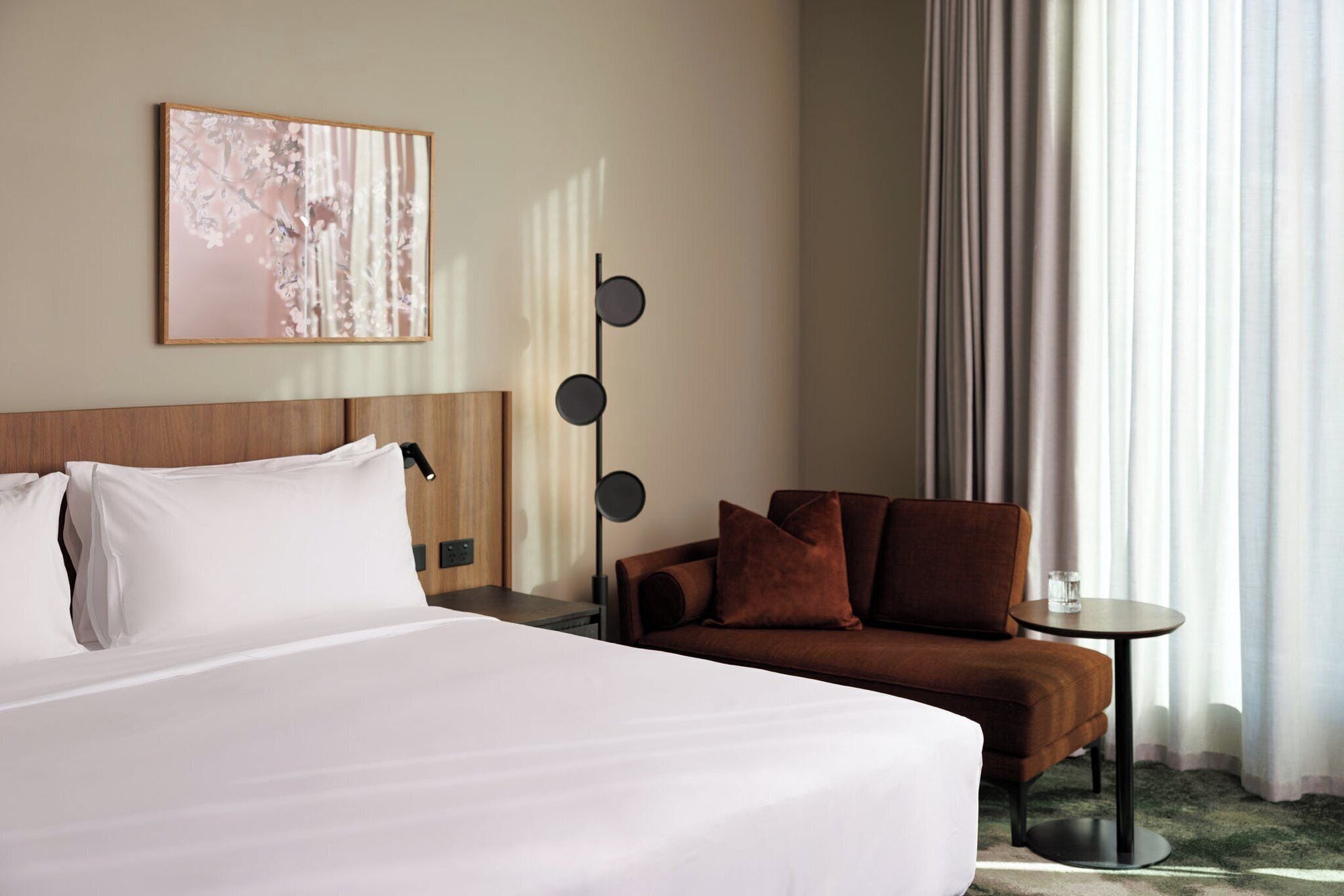 A hotel room with a large bed, a brown sofa, a small table, and a wall-mounted lamp.