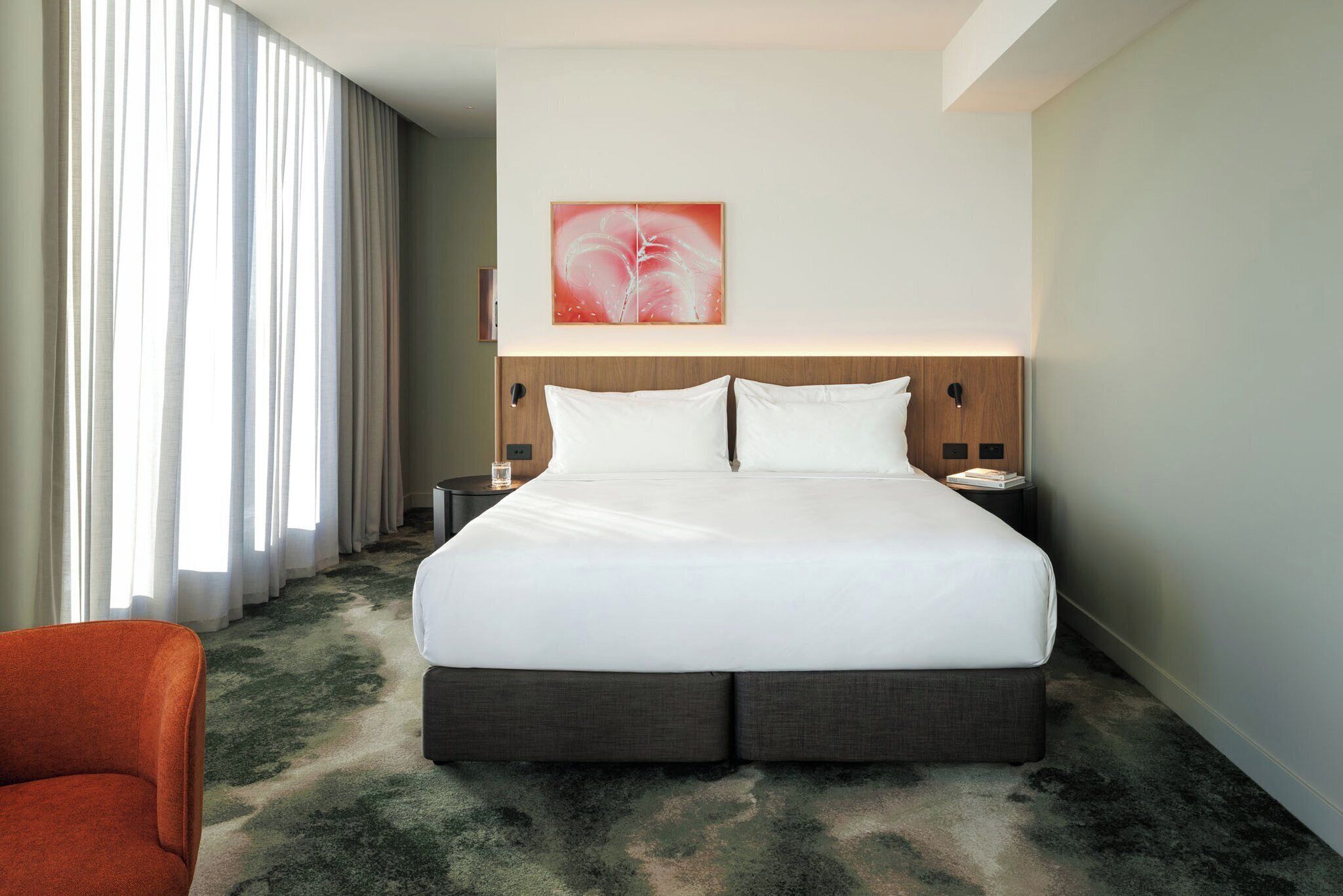 Una habitación de hotel con una cama grande, una mesita de noche, una silla y un cuadro en la pared.