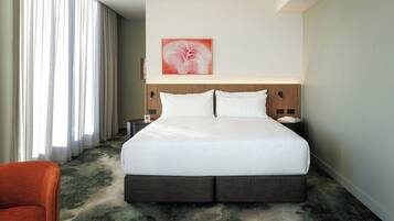 Una habitación de hotel con una cama grande, una mesita de noche, una silla y un cuadro en la pared.