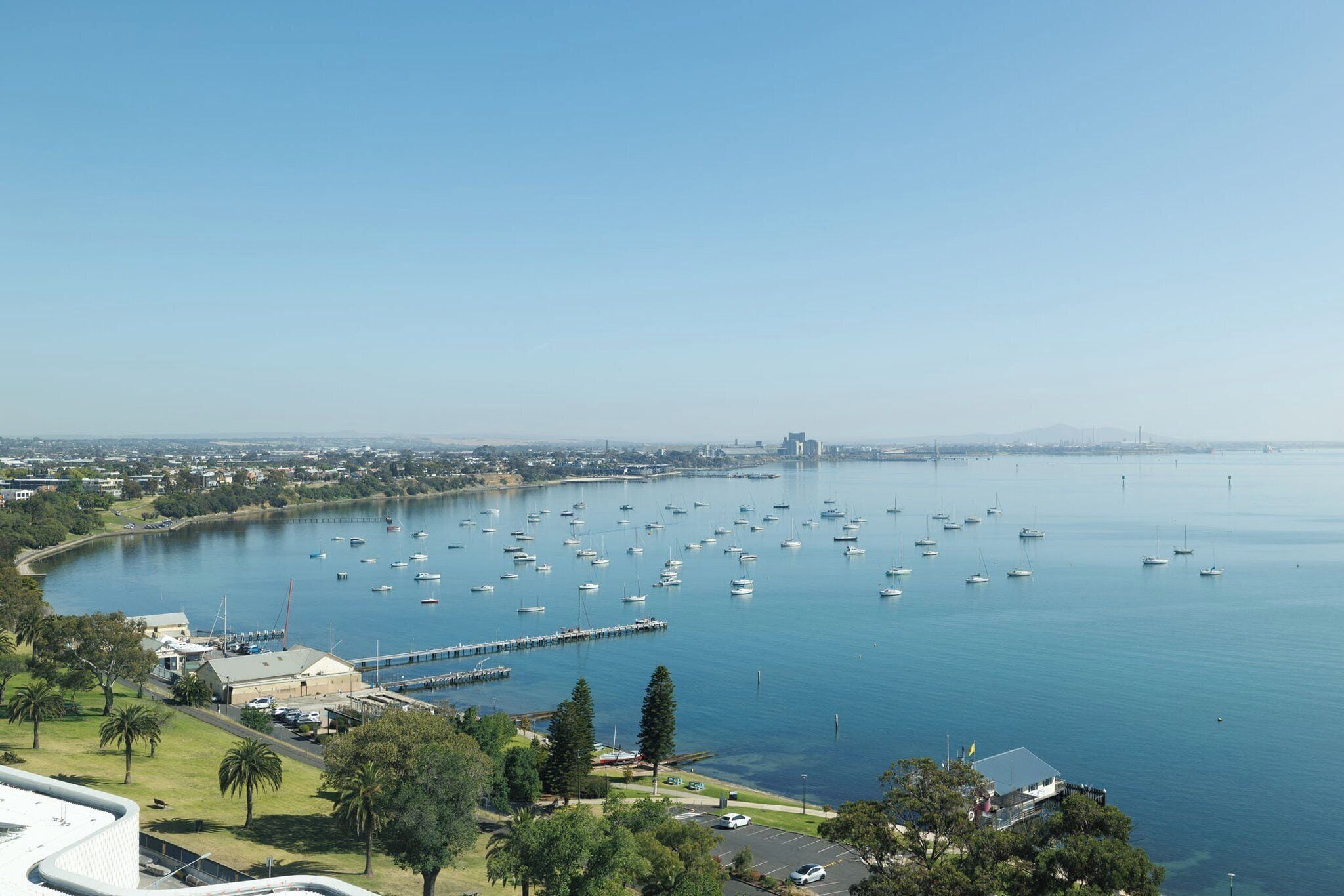 A marina with numerous boats docked, a clear sky, and a distant cityscape.
