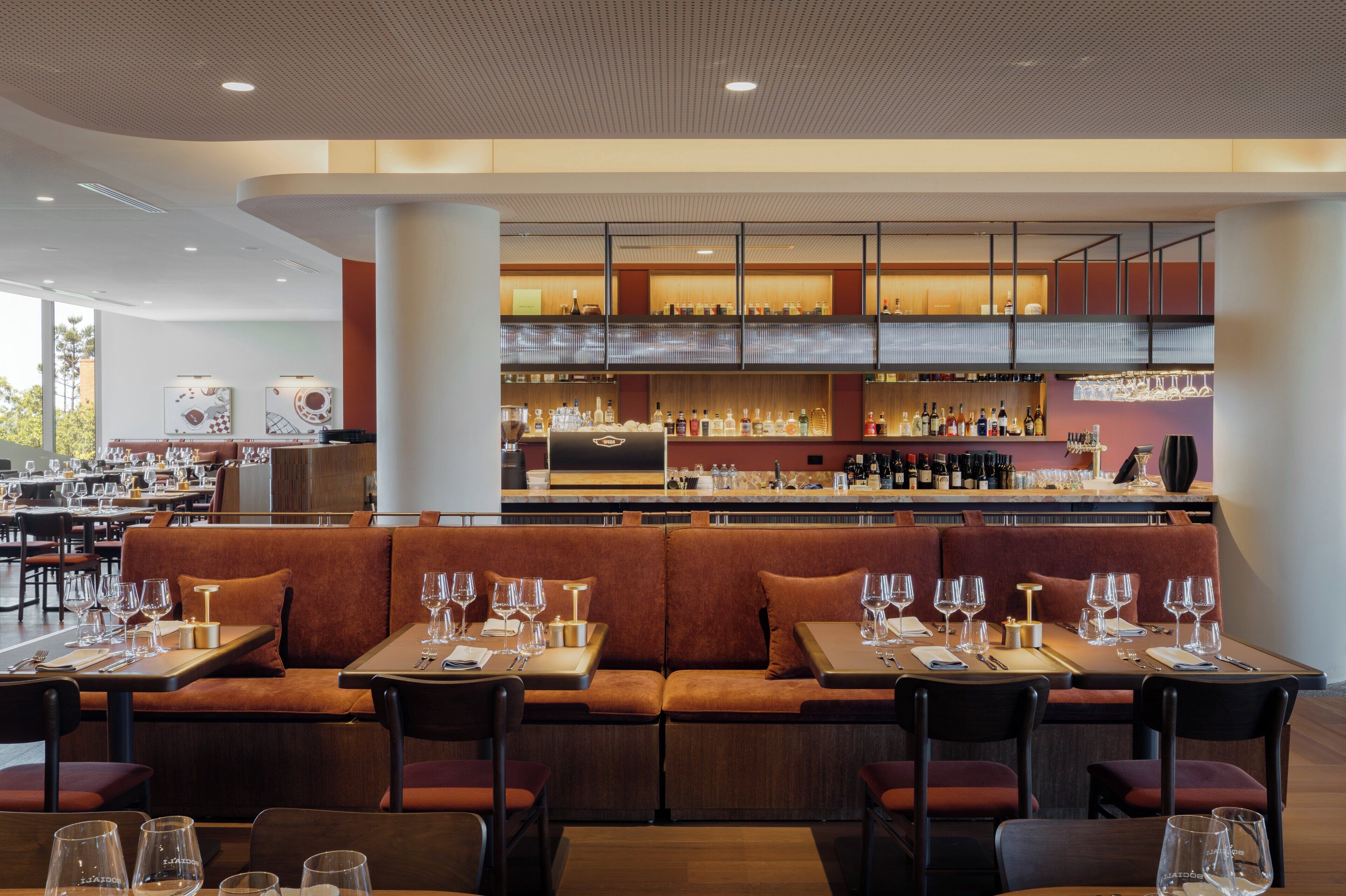 Un restaurant moderne doté d’un bar, de différents espaces pour s’asseoir et offrant une vue sur l’extérieur.