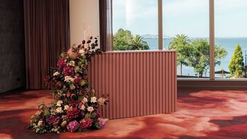 A room with a large window, a red carpet, and a floral arrangement on a podium.