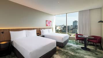 A hotel room with two beds, a city view, a red chair, and a small table.