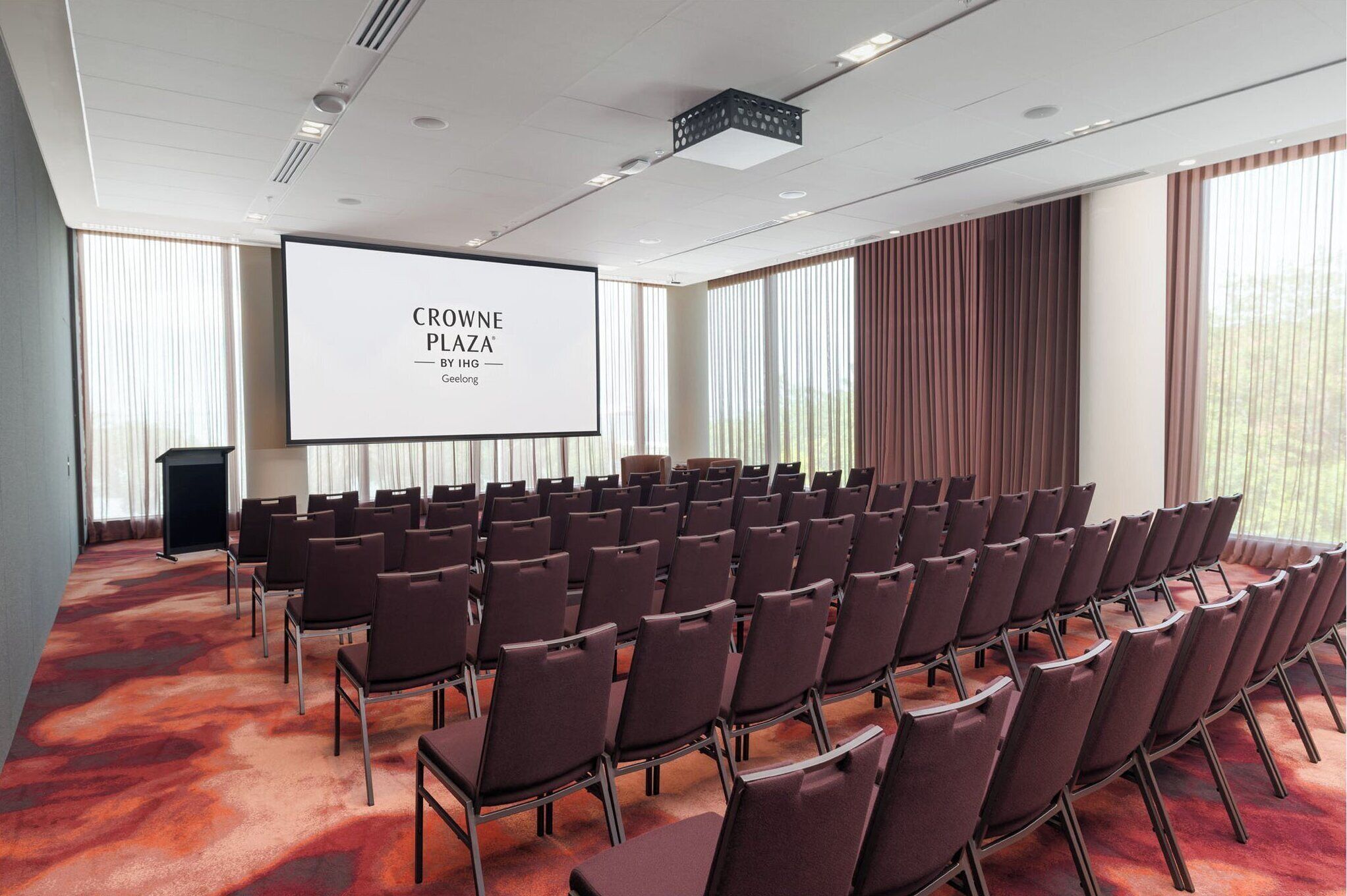 Una sala de conferències amb files de cadires, una pantalla de projector i un escenari.