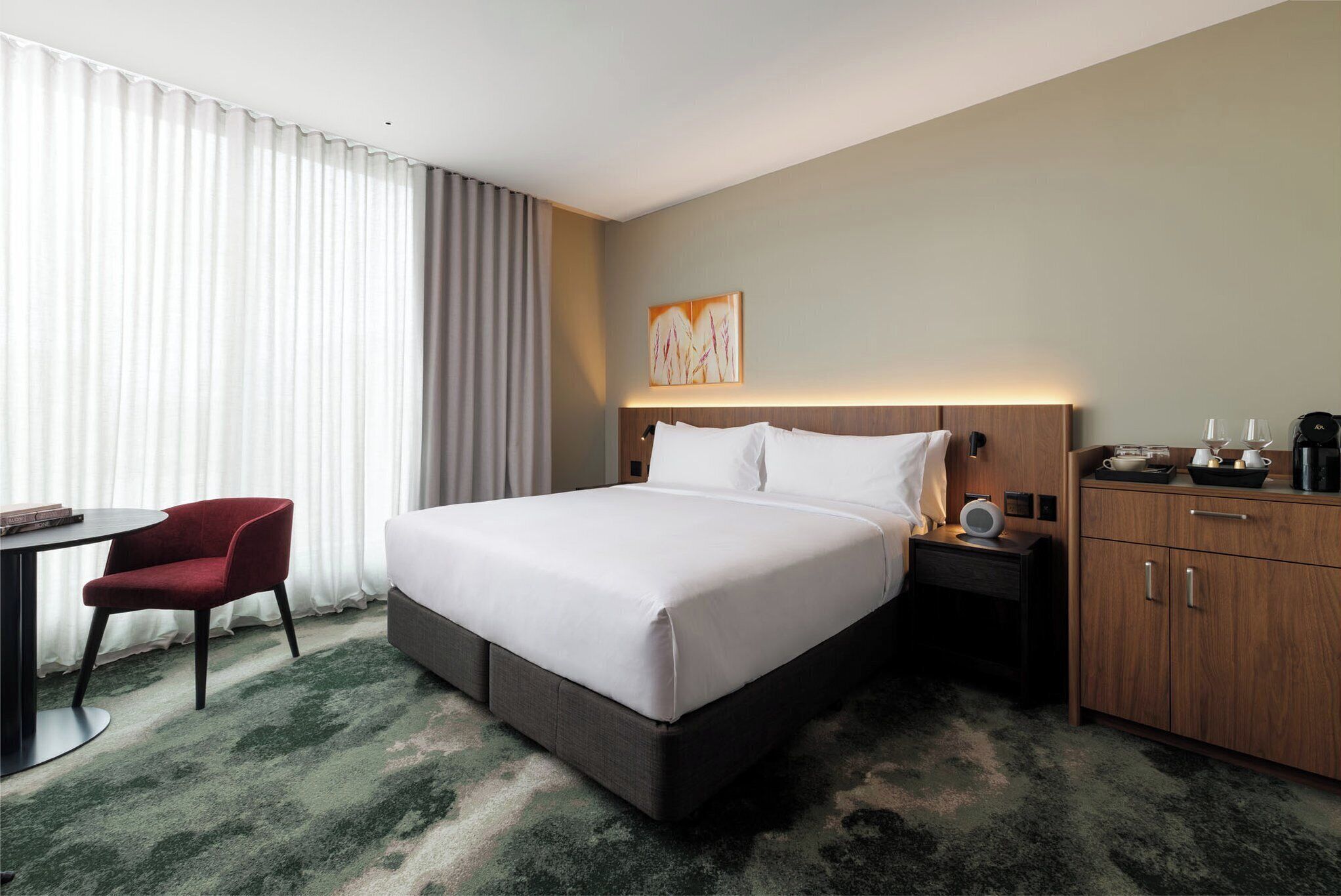 Habitación de hotel con una cama grande, un escritorio con silla, un armario de madera y un cuadro en la pared.