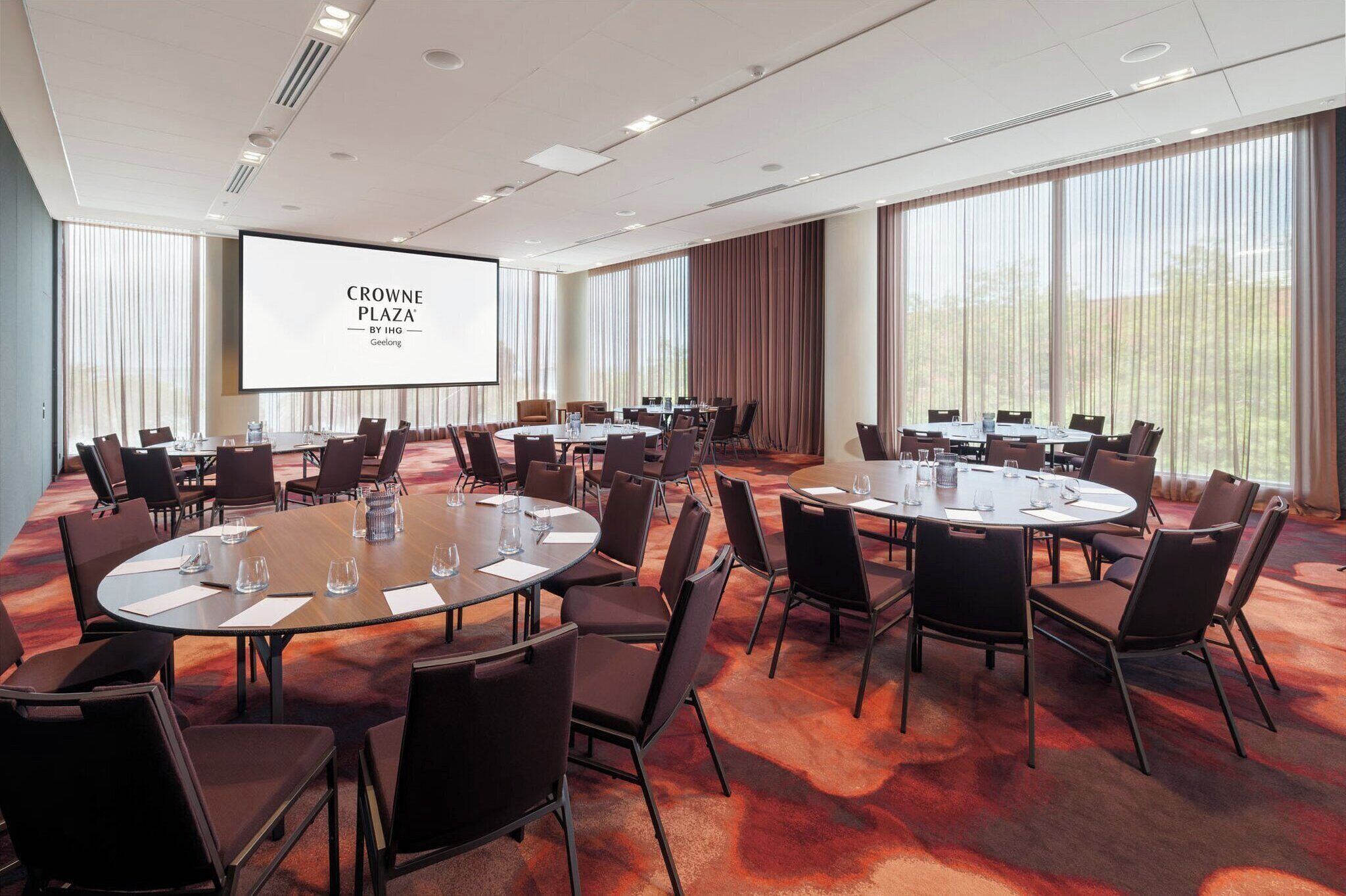 Un salón de conferencias con varias mesas redondas, sillas y una pantalla grande que muestra 