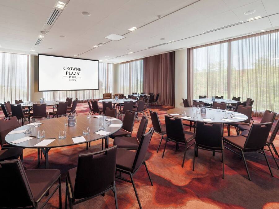 Un salón de conferencias con varias mesas redondas, sillas y una pantalla grande que muestra