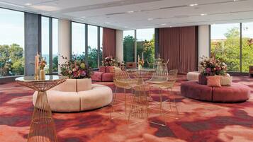 Una habitación de hotel moderna con ventanas amplias, alfombra roja, una mesa redonda con sillas y un sofá con una mesita auxiliar.