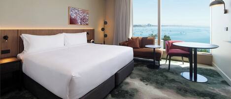 Habitación de hotel con una cama grande, un sofá, una mesita y vistas al mar.