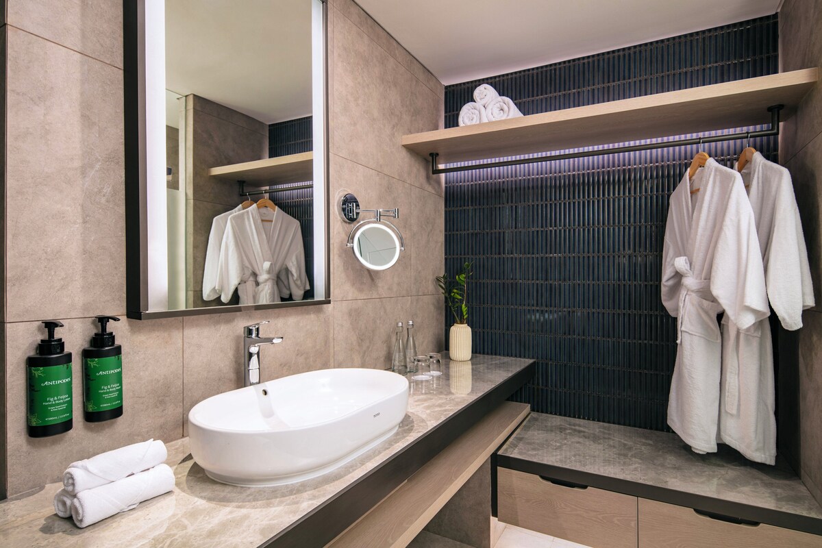 Un baño moderno con un lavamanos grande de color blanco, un espejo y dos repisas con toallas.