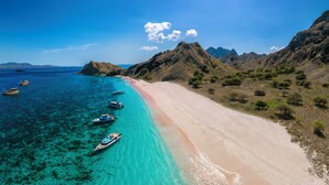 Eine Küstenlandschaft mit einem klaren Strand, Booten und gebirgiger Landschaft.