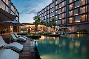 Un hotel moderno con piscina, sillones de descanso y sombrillas.