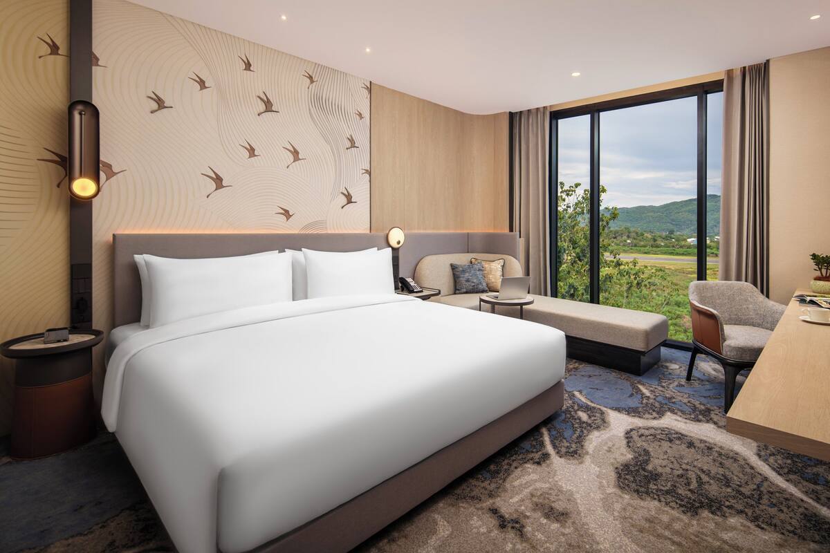Quarto de hotel moderno com uma cama grande, área de estar com vista e uma mesa de trabalho.
