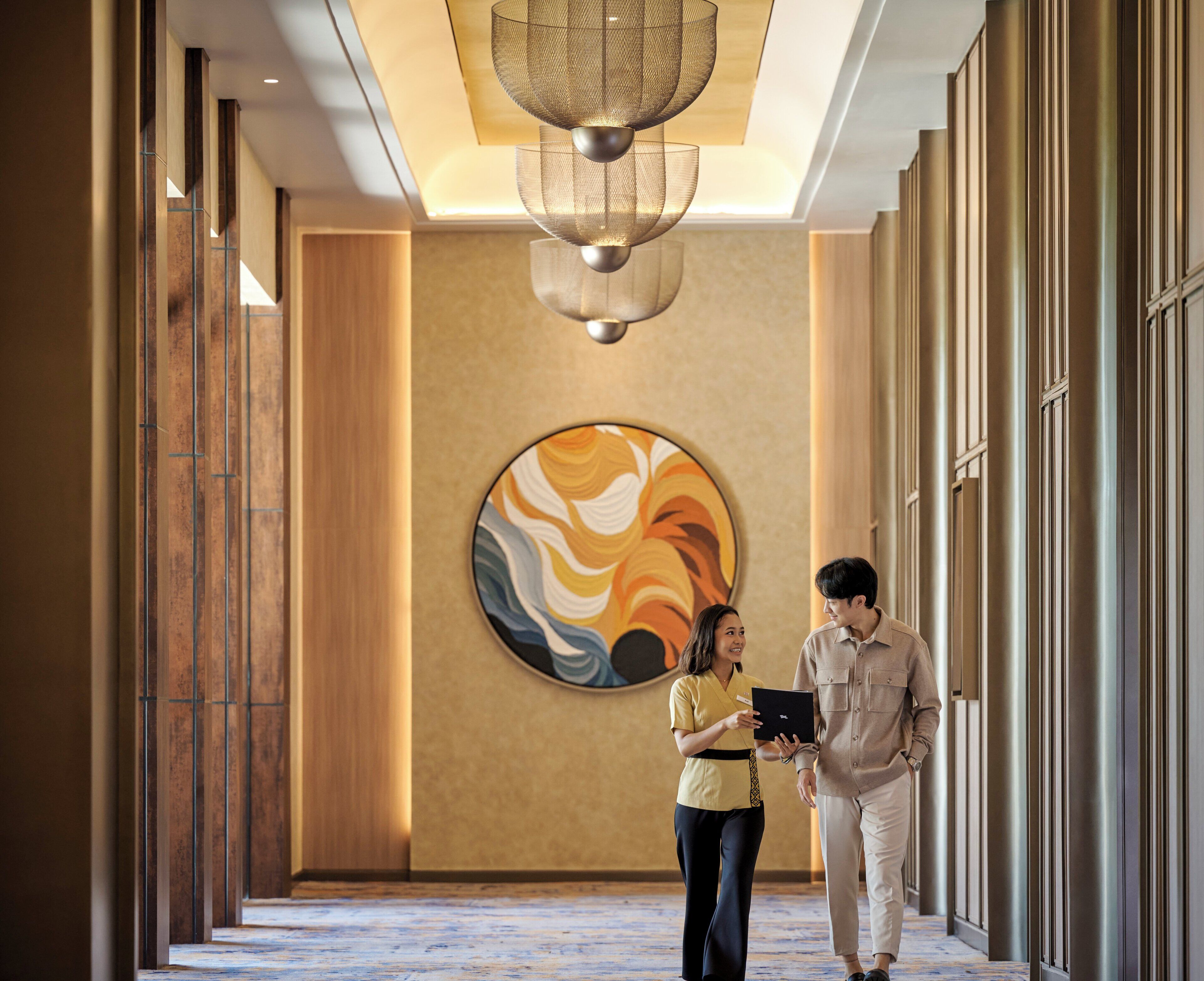 A hallway with a large abstract painting, a ceiling light fixture, and a person holding a tablet.