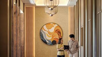 A hallway with a large abstract painting, a ceiling light fixture, and a person holding a tablet.