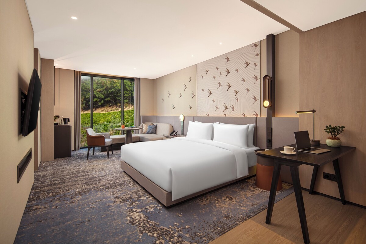 Una habitación de hotel moderna con una cama grande, un escritorio, una silla y un televisor.