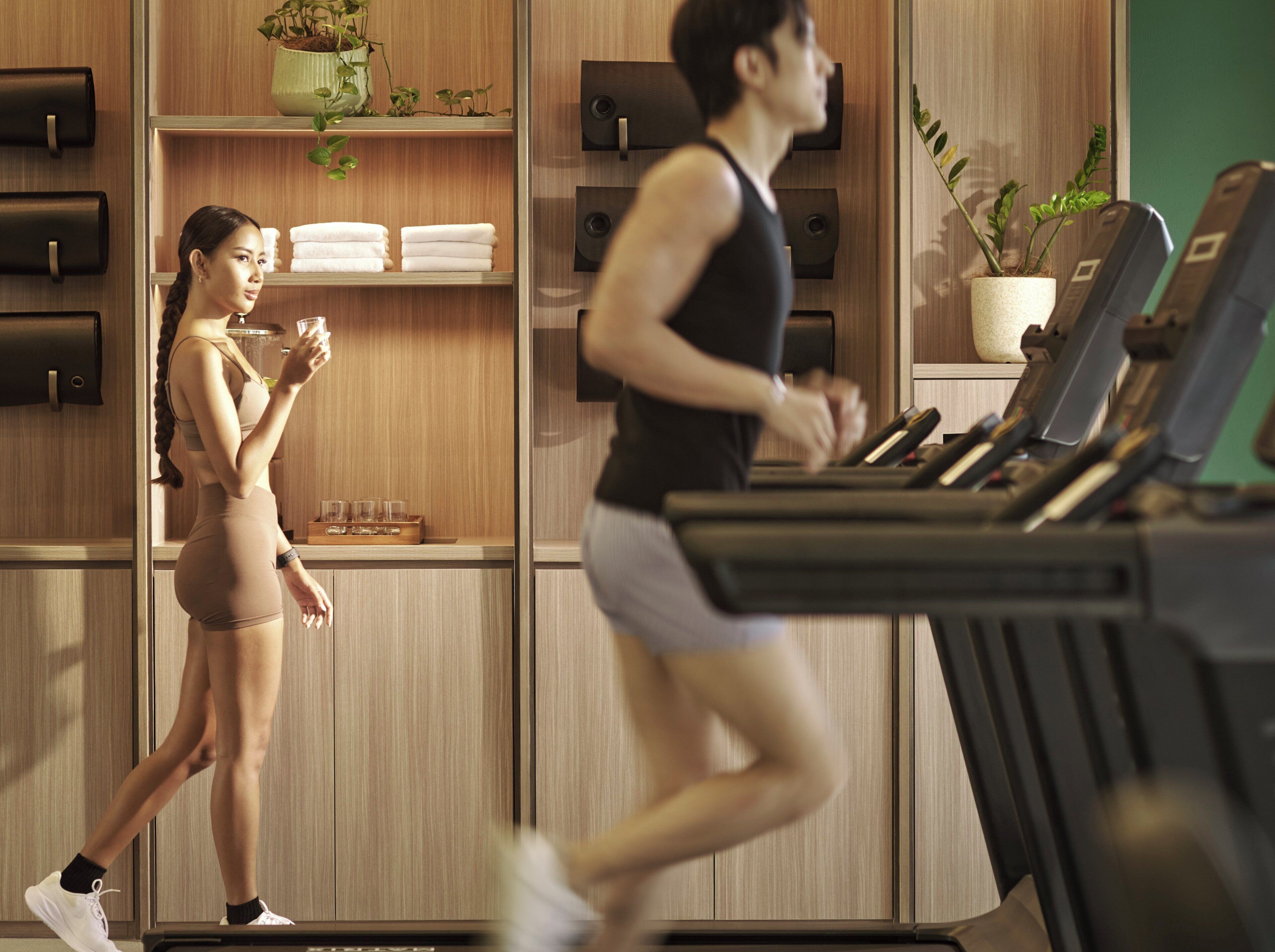 A gym with treadmills, a woman holding a glass, and a man running.