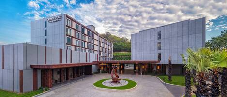 Un hotel moderno con un patio central, una escultura destacada y un letrero que dice "CROWNE PLAZA BY THG".