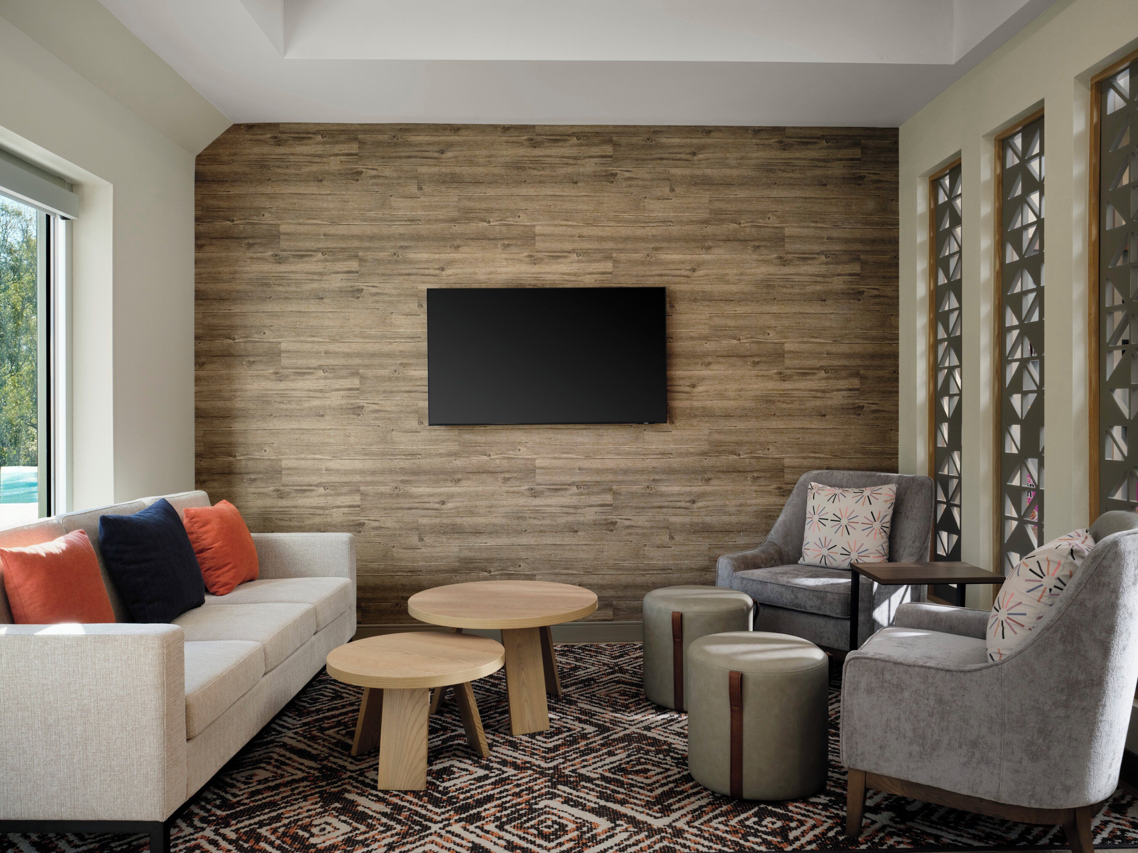 Un salon moderne avec un mur en bois, un téléviseur à écran plat, un canapé, deux tables rondes et un tapis à motifs.