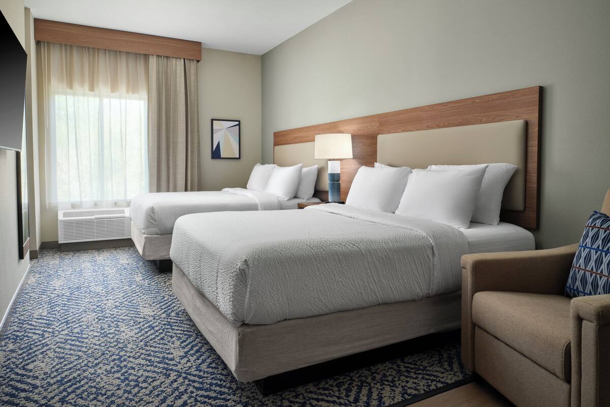 A hotel room with two beds, a desk, a chair, a lamp, and a window with curtains.