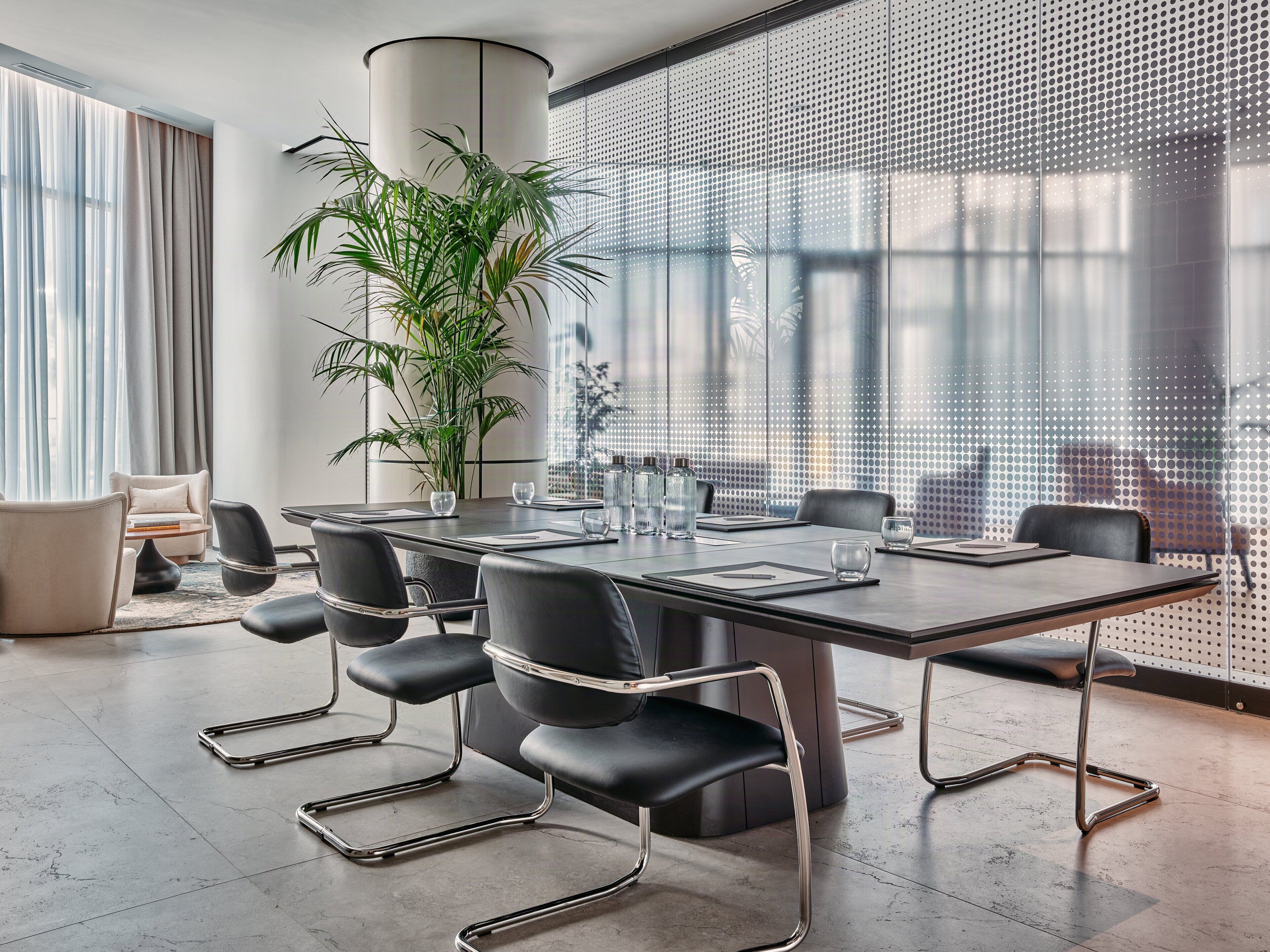 Une salle de réunion moderne, dotée d’une grande table, de chaises noires, d’une plante en pot et de grandes fenêtres au motif ajouré.