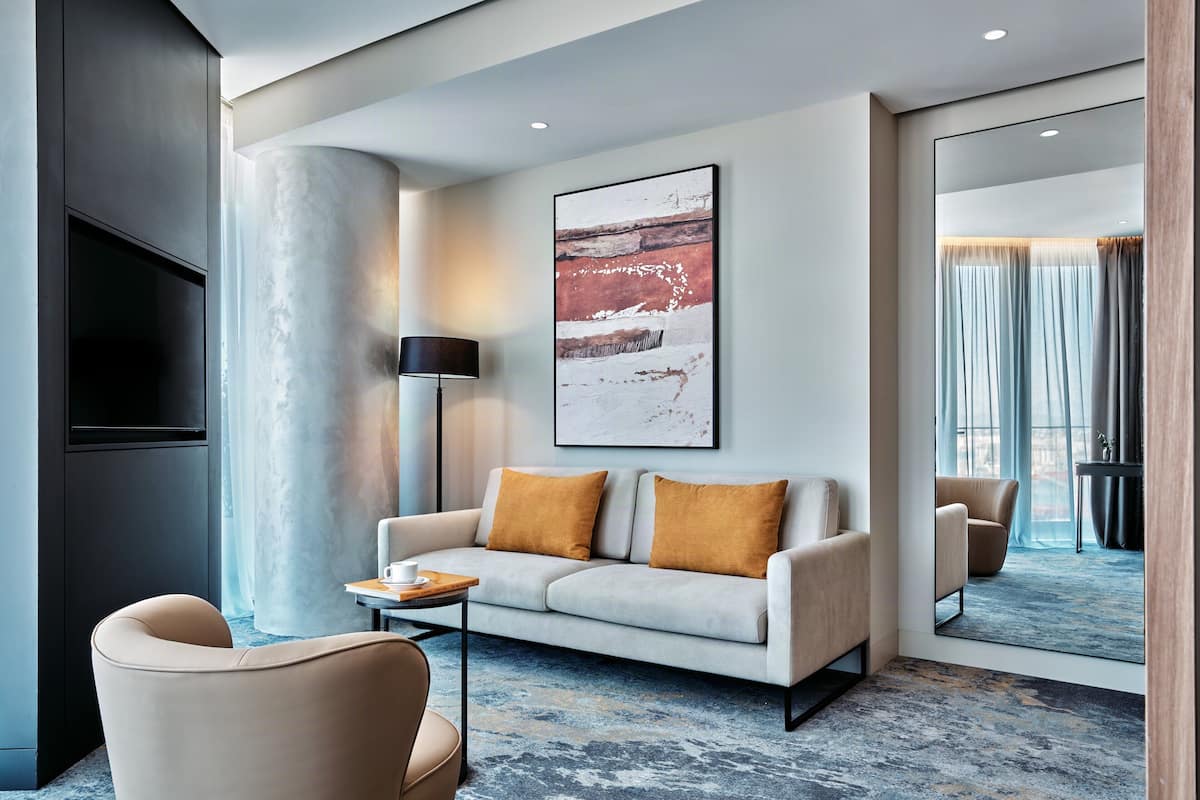 Een moderne hotelkamer met een bank, fauteuil, salontafel en een grote spiegel die de kamer weerspiegelt.