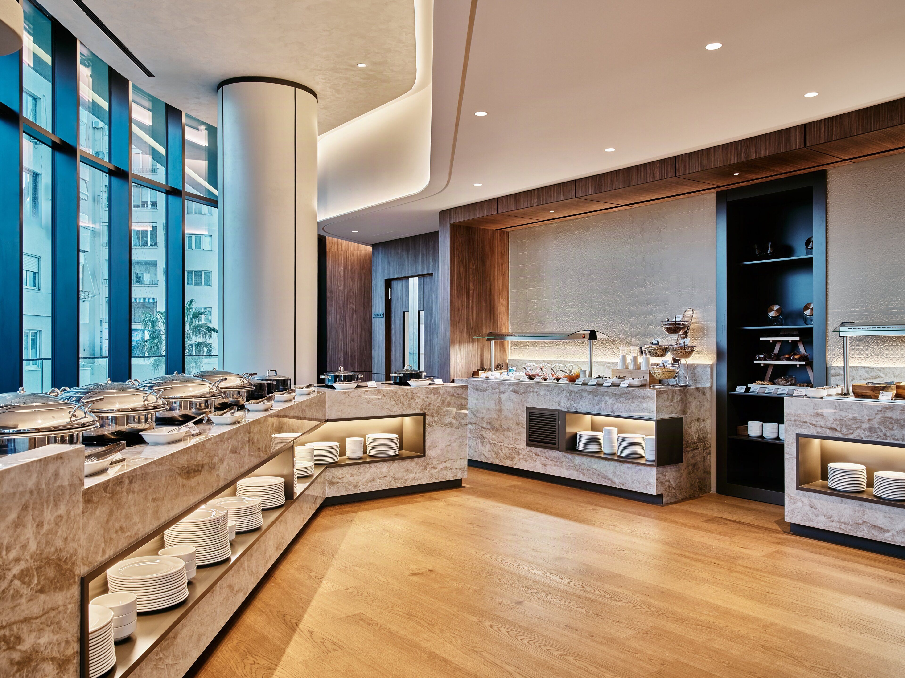 Un'accogliente hall d'hotel moderna con una scrivania della reception in marmo, un'area buffet e ampie finestre che offrono vista sulla città.