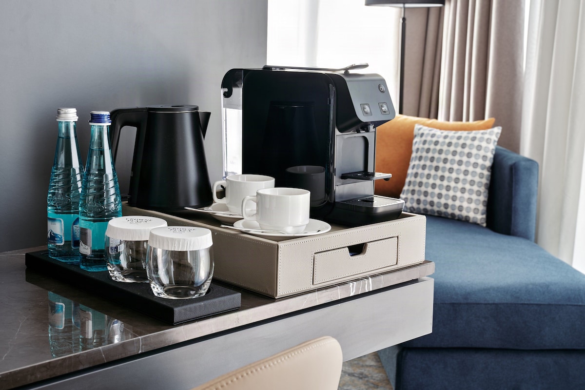 A hotel room with a coffee maker, water bottles, glasses, and a sofa.