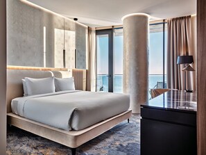 Une chambre d’hôtel moderne, dotée d’un grand lit, d’un bureau et offrant une vue sur la mer.