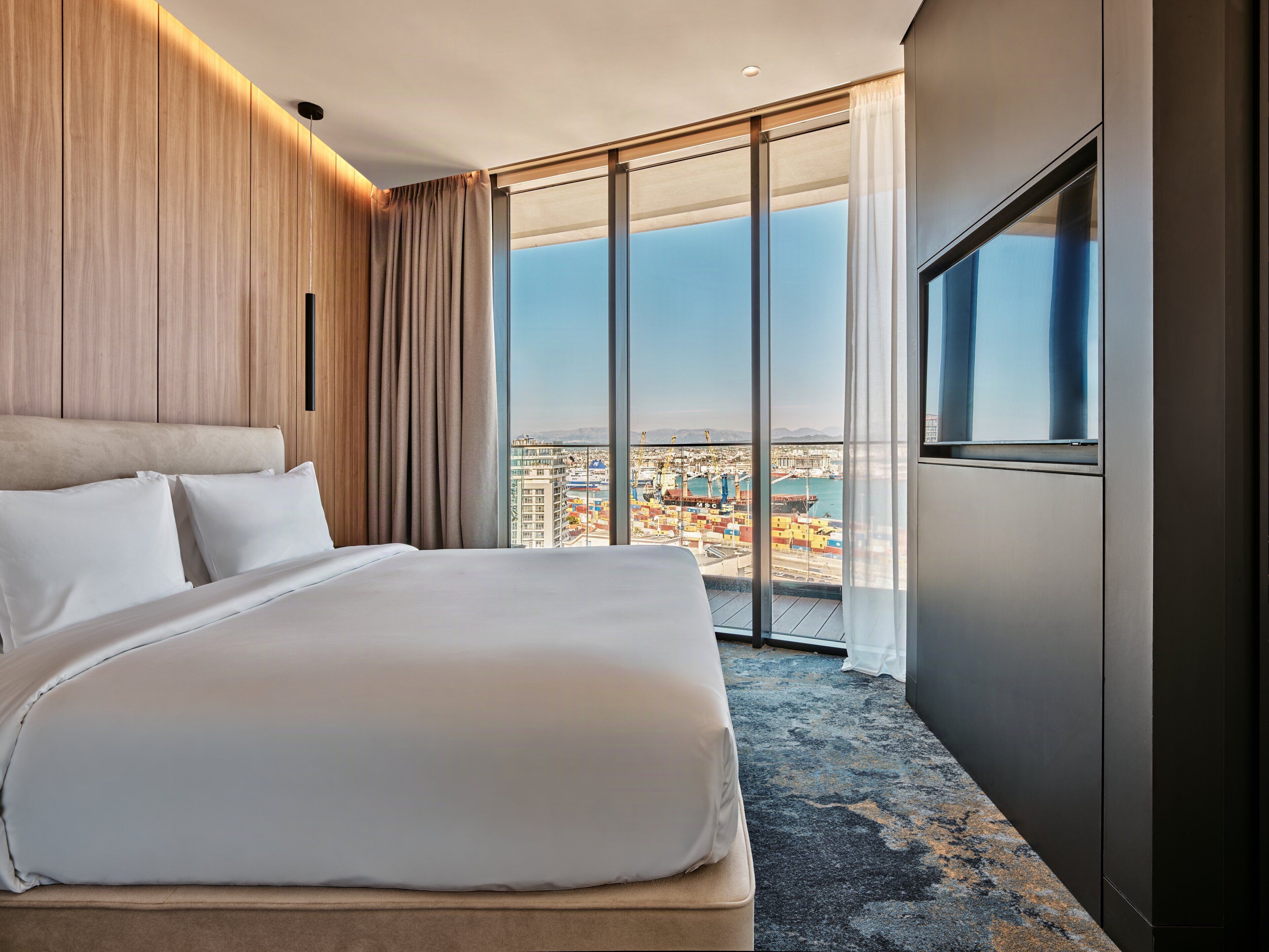 A hotel room with a large bed, a view of a port, and a cityscape.
