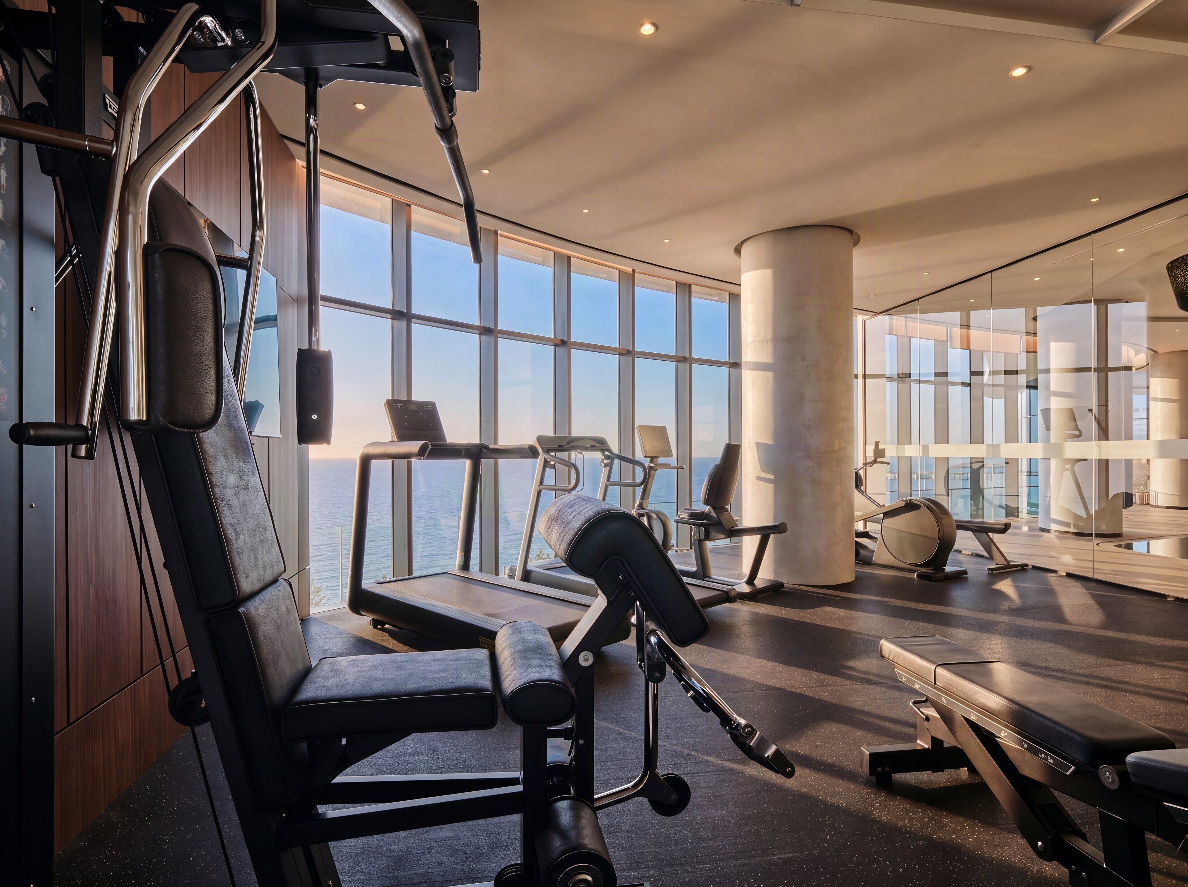Et moderne fitnesscenter med træningsudstyr, store vinduer og havudsigt.