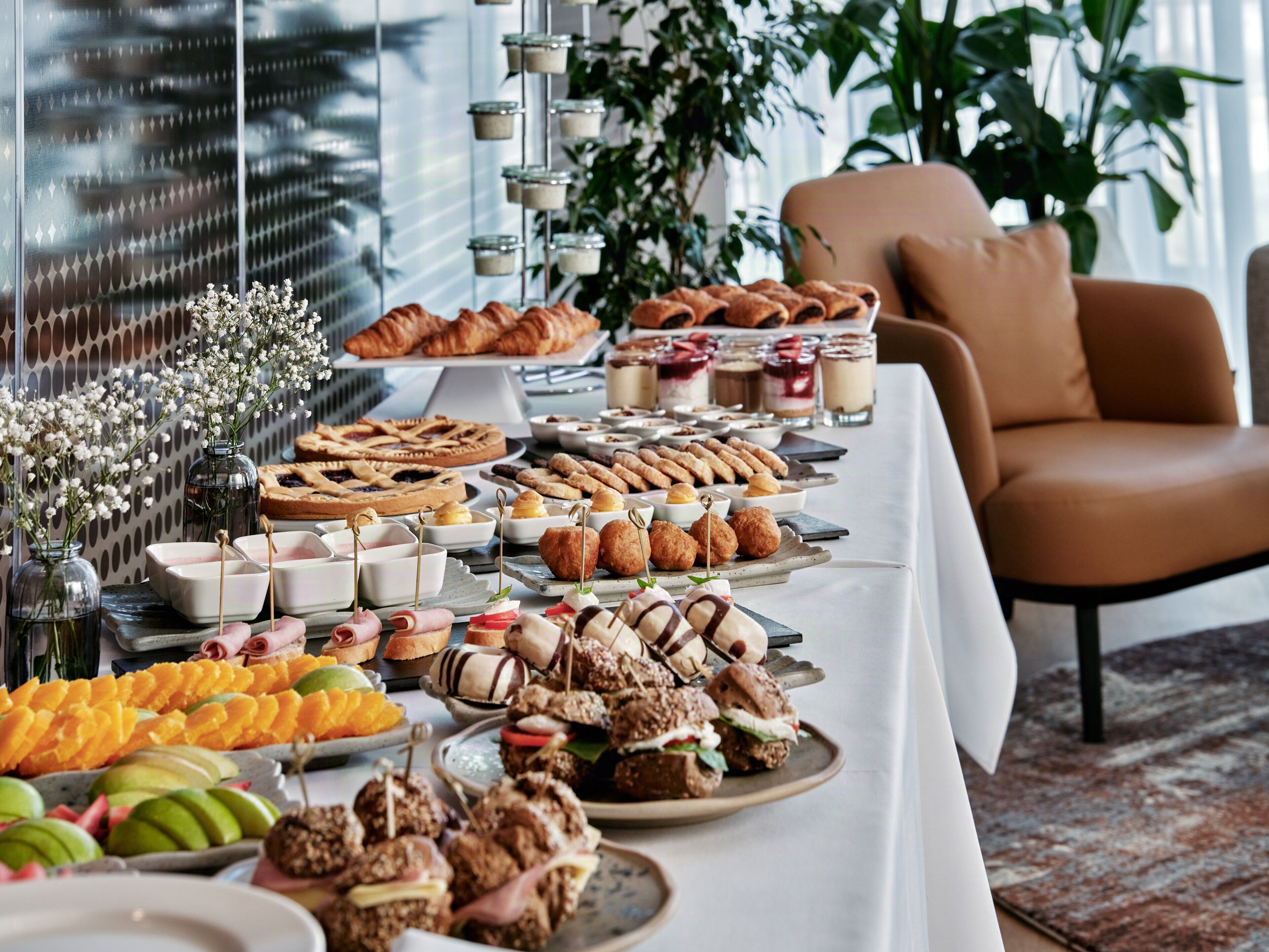 A buffet table with various food items, a chair, and a plant in the background.