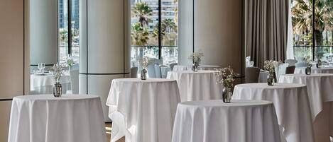 A hotel dining area with round tables, white tablecloths, and vases of flowers.