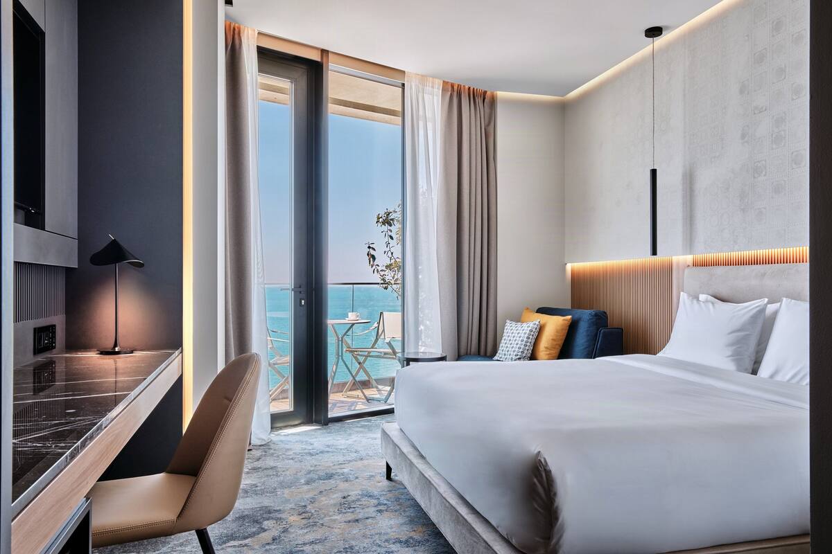 Ein Hotelzimmer mit Bett, Schreibtisch, Sessel, Fernseher und einem Balkon mit Blick.