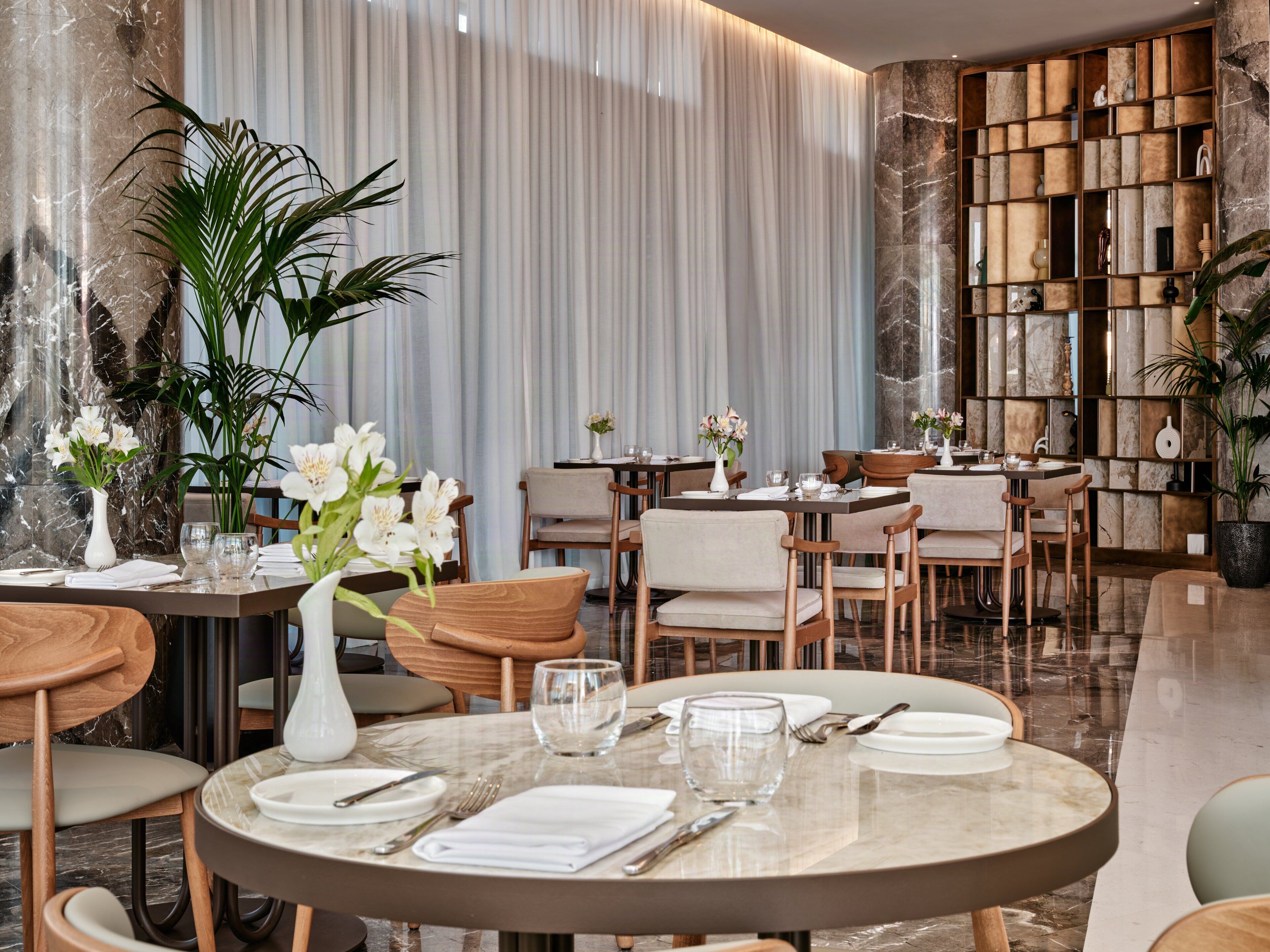 A restaurant with marble walls, wooden furniture, and white flowers on tables.