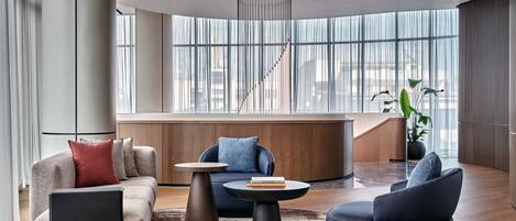 Een moderne woonkamer met een bank, fauteuil, salontafel en een groot raam met uitzicht op de stad.