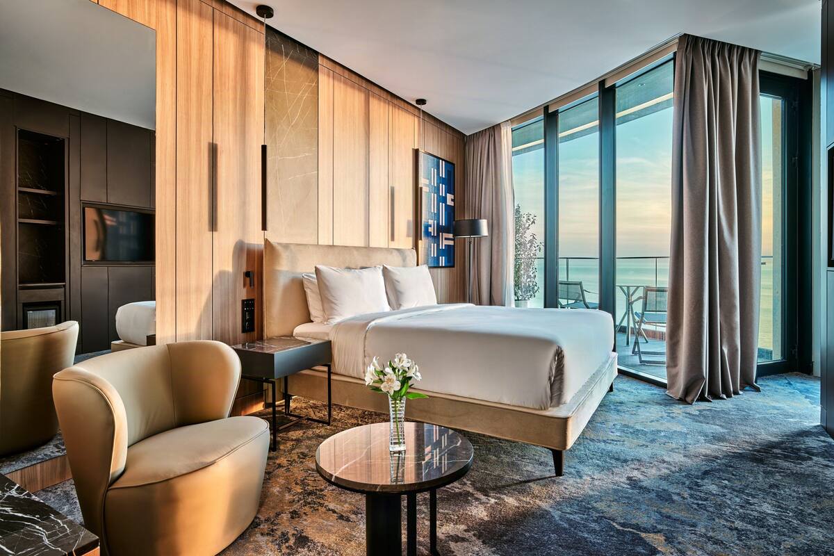 Een moderne hotelkamer met een groot bed, een zithoek met een salontafel, een televisie en een balkon met uitzicht.