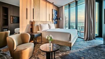 Una habitación de hotel moderna con una cama grande, una zona de estar con una mesita de café, un televisor y un balcón con vistas.