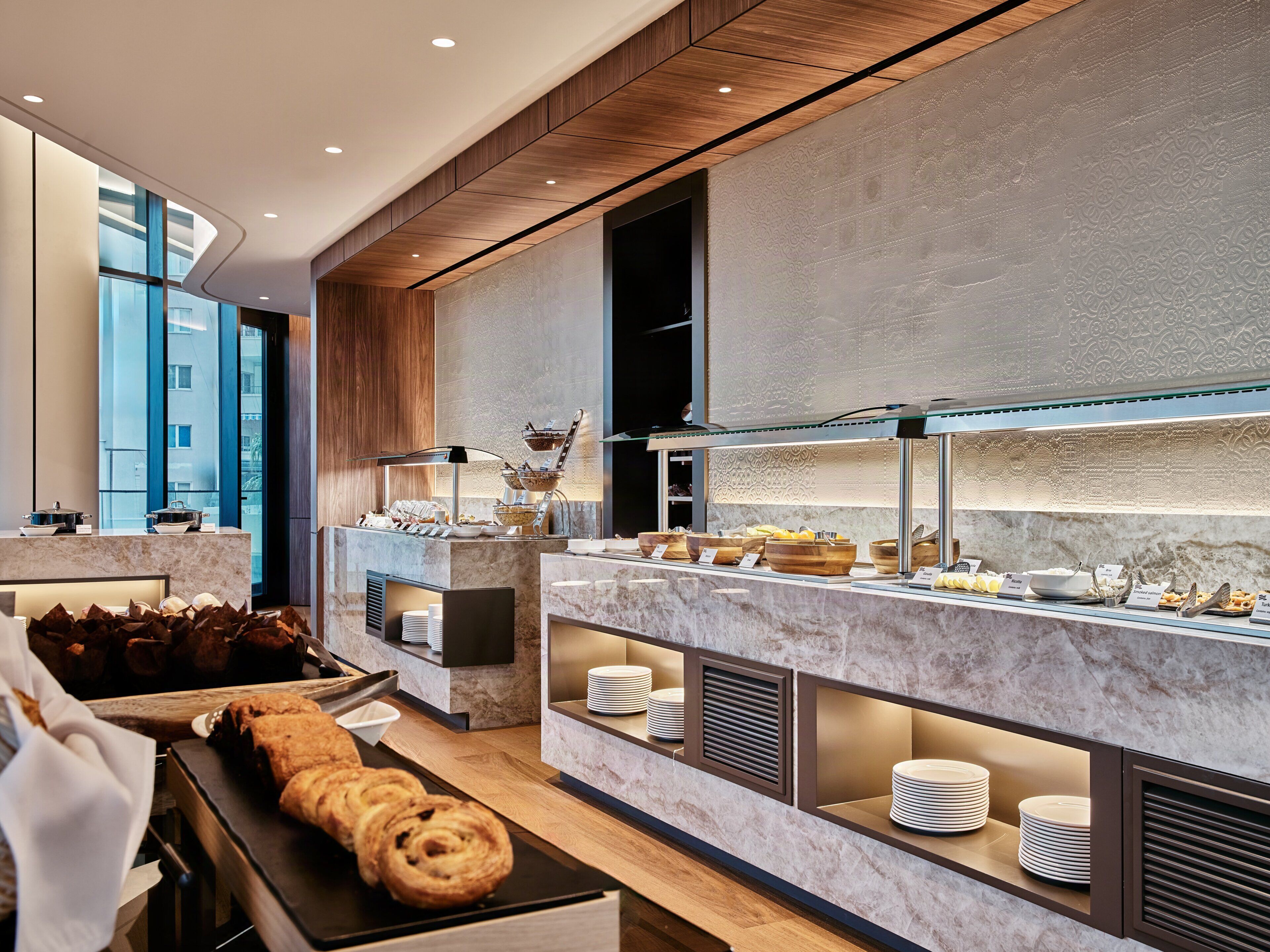 A modern breakfast buffet with marble counters, a variety of food items, and a large pastry display.
