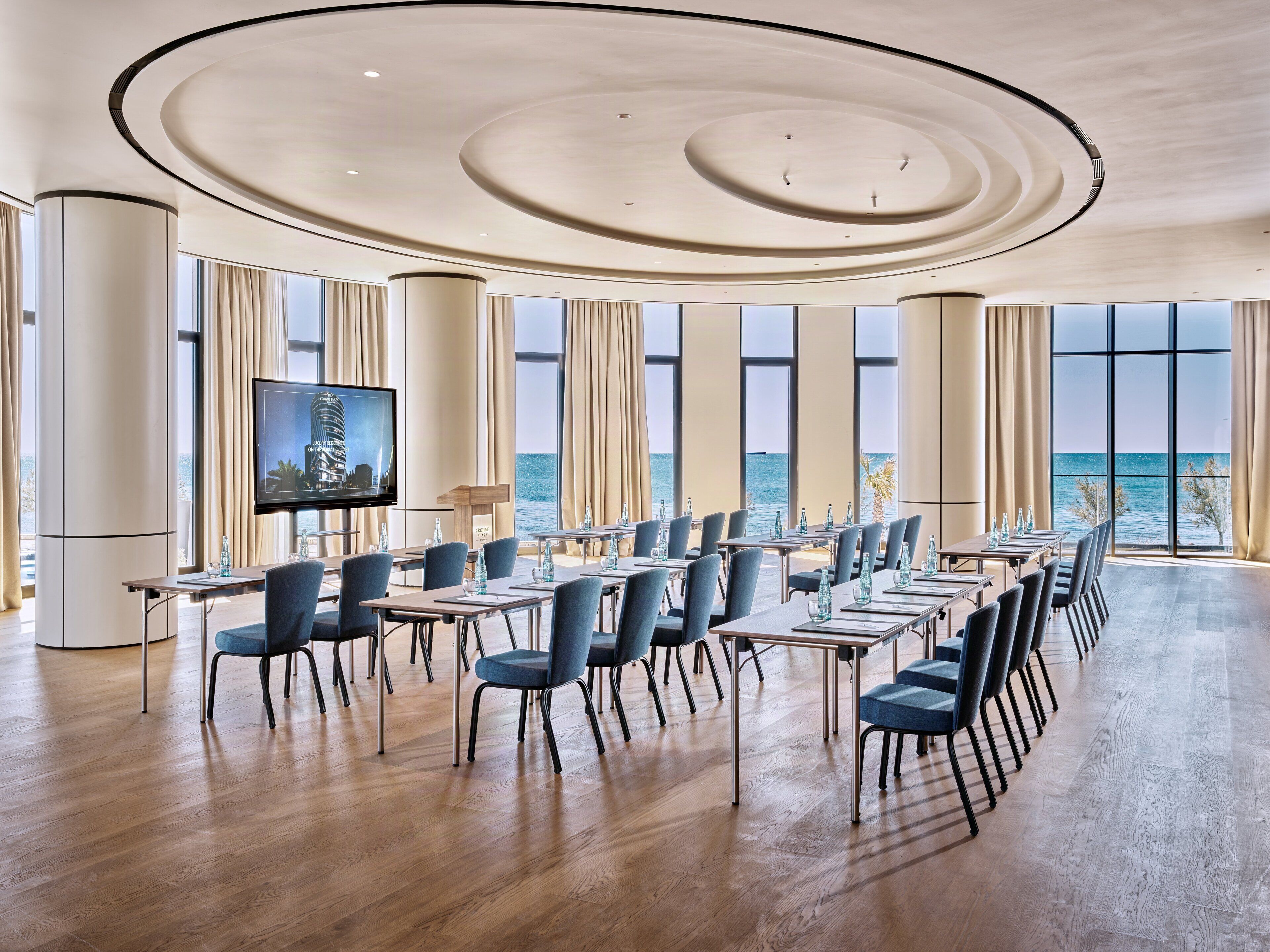 Un salón de conferencias con amplia vista al mar, pisos de madera y sillas modernas.