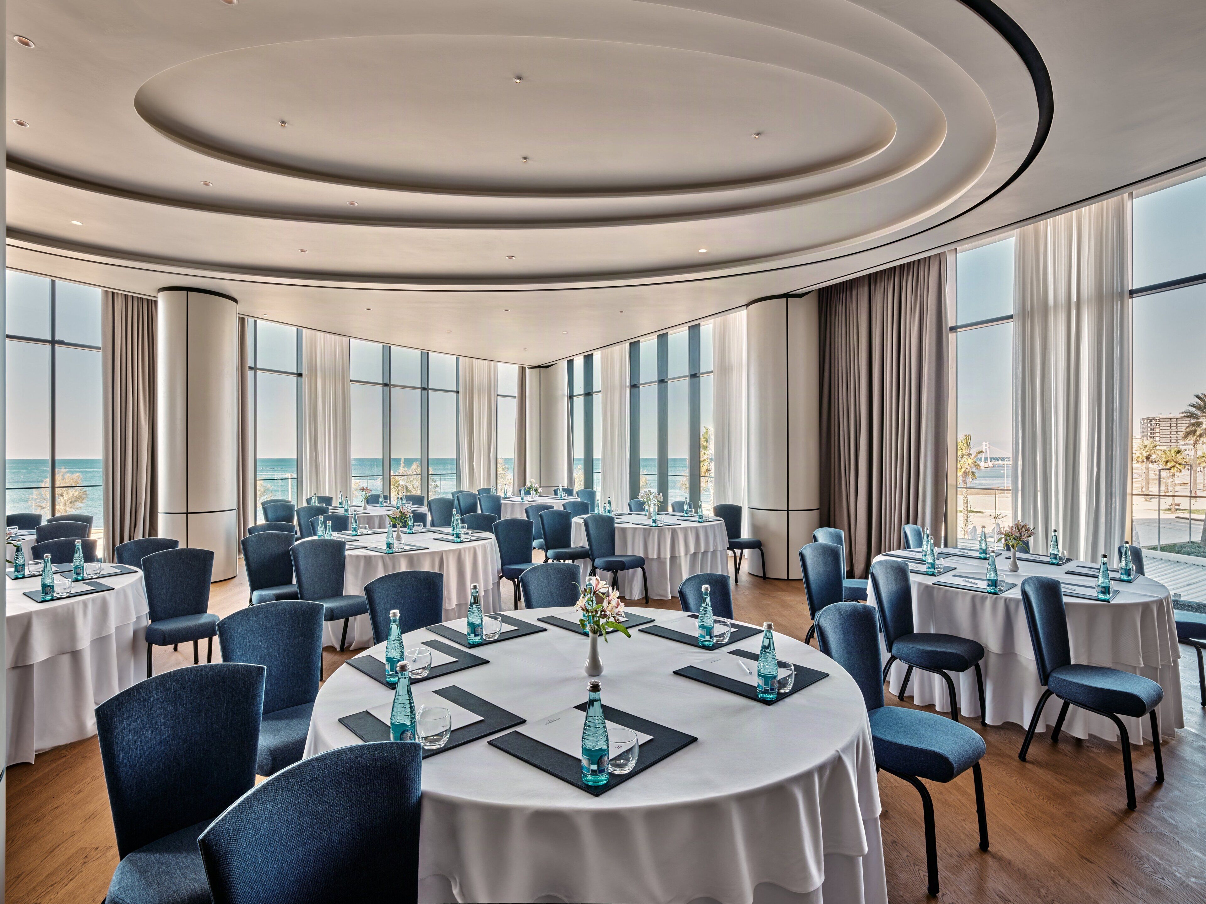 A conference room with round tables, chairs, and a view of the sea.