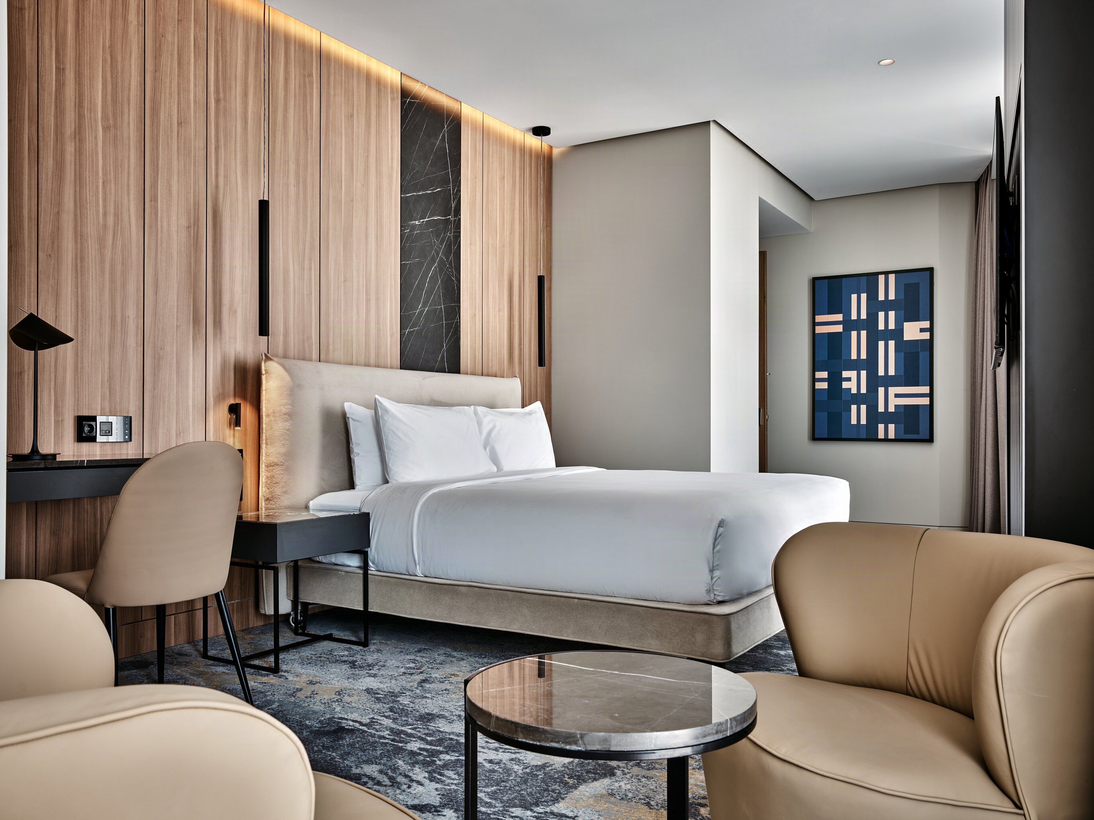 Ein modernes Hotelzimmer mit einem Bett, zwei Stühlen, einem kleinen Tisch, einem Schreibtisch und einem Wandbild.