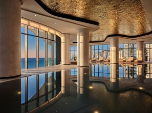 Un interior moderno con una piscina reflectante, ventanas amplias y sillones de descanso.